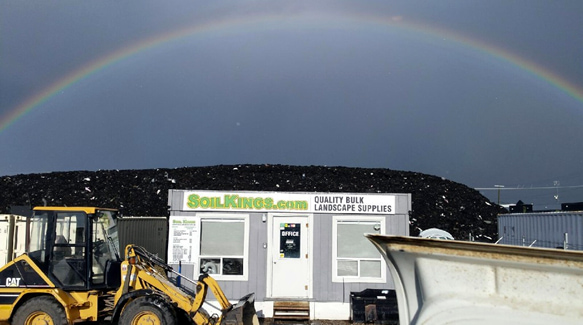 Soil Kings office with heavy equipment and bulk soil piles at landscaping supply facility.