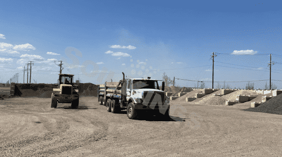 Dump truck and loader transporting bulk soil and aggregates at construction supply yard.