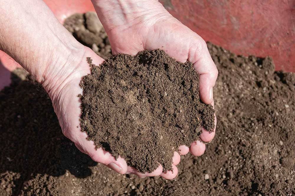 Person adding adding screened topsoil to lawn using their hands