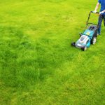 A man mows a green lawn on a sunny day. It's spring, and he's taking care of his yard.