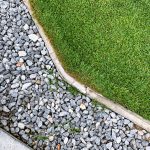 Practical use of drain rock in landscaping around a green lawn.