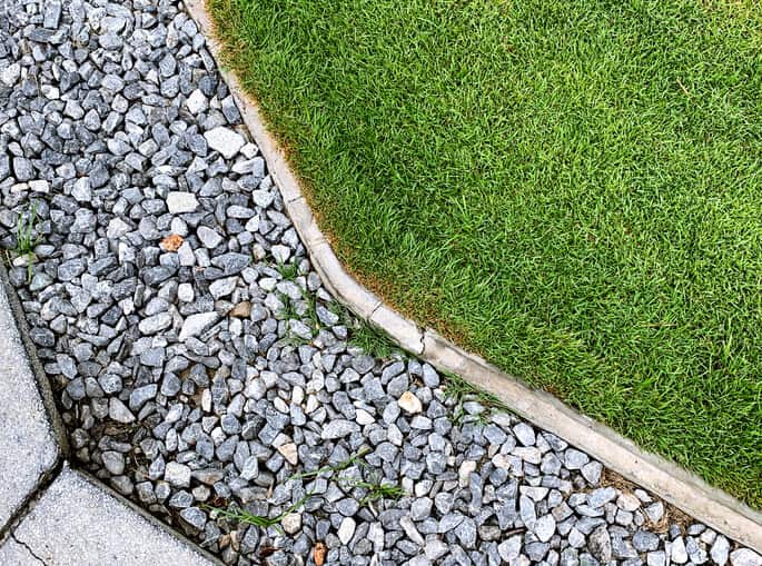 Practical use of drain rock in landscaping around a green lawn.
