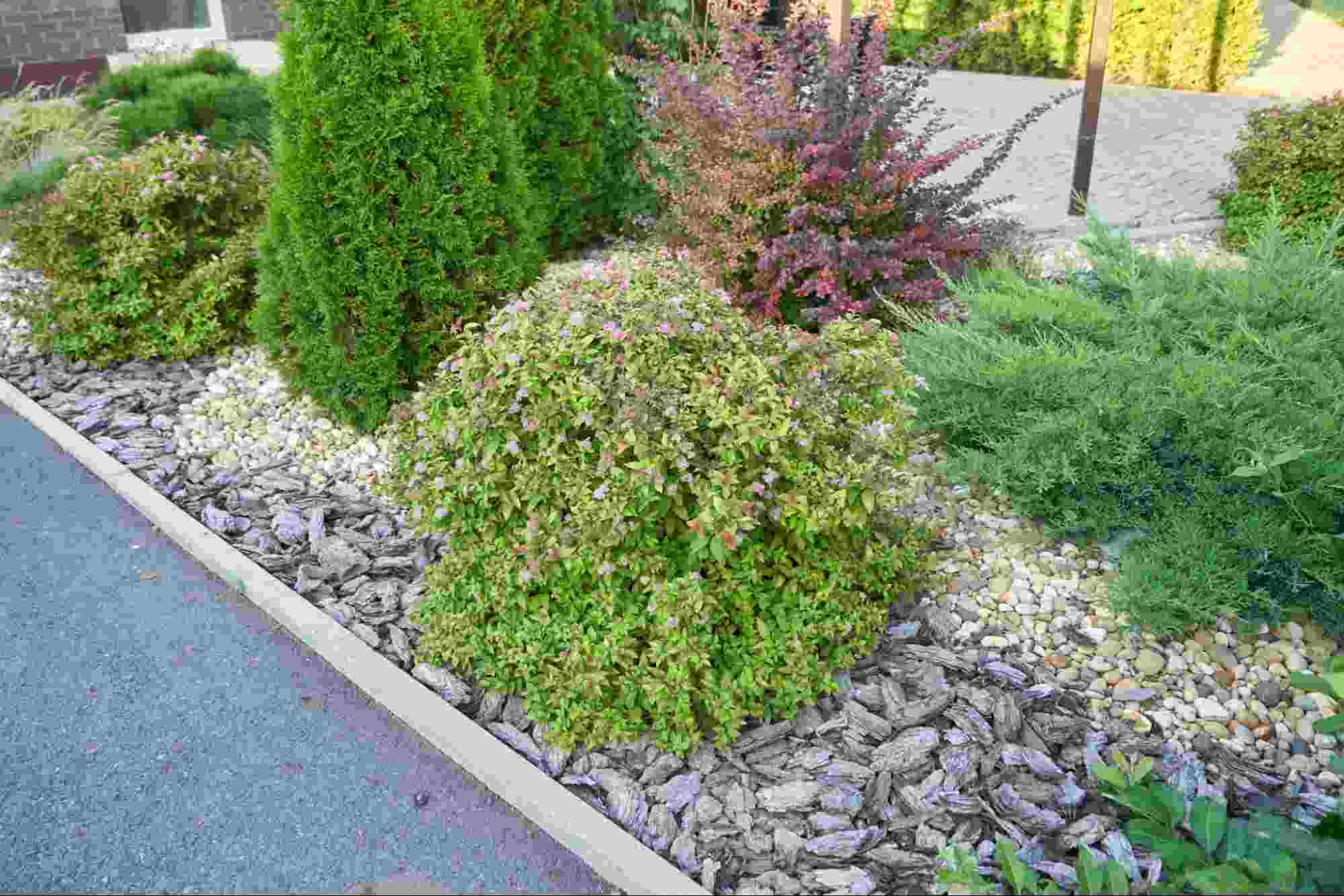 Rundle rock installed in a landscaped garden bed with ornamental shrubs and evergreen plants, showcasing the durability and visual appeal of rundle rock for residential landscaping projects.